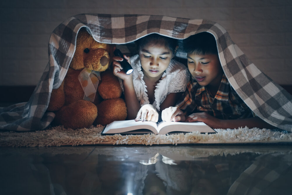 Happy children boy and girl reading a book in blanket at home with a toy treddy bear Photo: AdobeStock